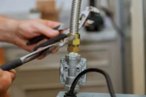 Close-up of hands using a wrench to tighten a brass fitting on a flexible metal hose connected to a valve.