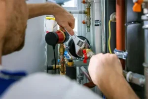 A person uses a wrench to tighten fittings on a network of pipes, focusing on a red valve in an industrial setting.
